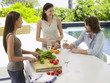 Three young adult friends preparing a salad while drinking wine and laughing on patio
