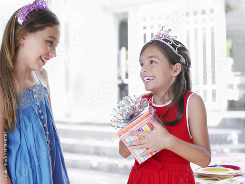 Photo: Two girls 7-9, 10-12 at birthday party, one holding present, smiling Two girls 7-9, 10-12 at birthday party, one holding present, smiling