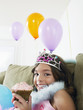 Foto: Young girl 7-9 sitting on sofa eating cupcake, close-up Young girl 7-9 sitting on sofa eating cupcake, close-up