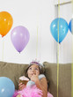 Foto: Young girl 7-9 sitting on sofa eating cupcake, looking up at balloons Young girl 7-9 sitting on sofa eating cupcake, looking up at balloons
