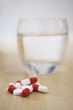 Pile of pills and glass of water on table, close-up