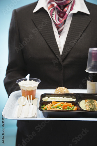 Photo: Stewardess holding tray with airplane food, mid section Stewardess holding tray with airplane food, mid section