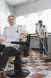 Two barbers in barber shop, one sweeping floor