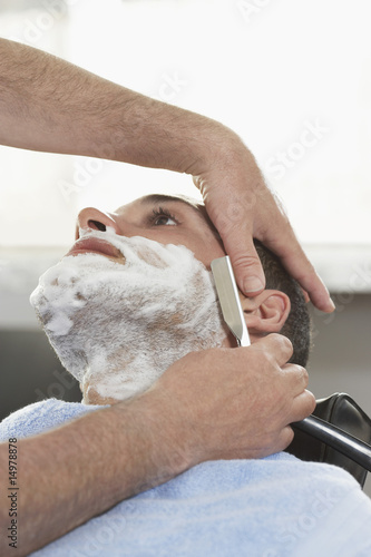 Foto: Barber shaving man in barber shop, close-up Barber shaving man in barber shop, close-up
