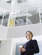 Photo: Business woman holding cup of coffee, standing in atrium of office building, low angle view Business woman holding cup of coffee, standing in atrium of office building, low angle view