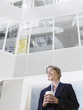 Photo: Business woman holding cup of coffee, standing in atrium of office building, low angle view Business woman holding cup of coffee, standing in atrium of office building, low angle view