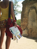 Photo: Young woman looking at ancient ruins, holding guide book, back view, mid section Young woman looking at ancient ruins, holding guide book, back view, mid section