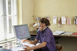 Young man reading papers and using phone in office