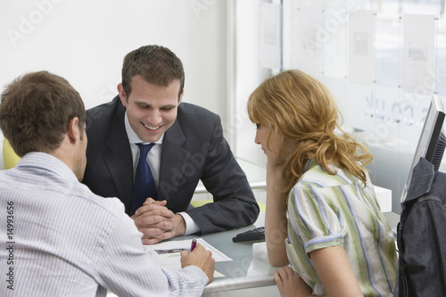 Photo: Couple with real estate agent in office, man writing Couple with real estate agent in office, man writing