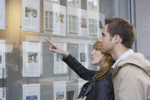 Photo: Couple looking in window outside estate agents Couple looking in window outside estate agents