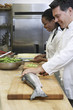 Male chef preparing salmon beside colleague in kitchen