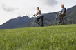 Man and woman biking, mountain range in background