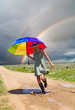 Girl with a rainbow umbrella splashing water in a puddle