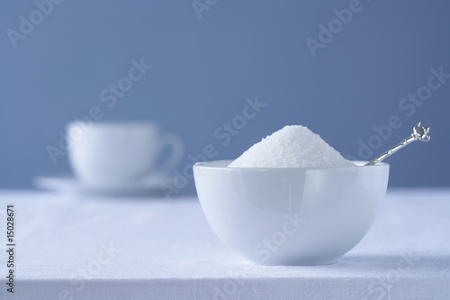 Photo: Bowl of sugar on table, tea cup in background Bowl of sugar on table, tea cup in background