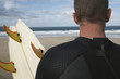 Man holding surfboard on beach looking at sea, back view, close up