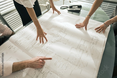 Photo: Closeup of professionals looking at architectural plans on desk Closeup of professionals looking at architectural plans on desk