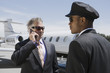 Photo: senior businessman standing outside private jet and talking on phone chauffeur assisting. senior businessman standing outside private jet and talking on phone chauffeur assisting.