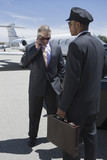 Photo: Senior businessman standing outside private jet and talking on phone, Chauffeur holding his suitcase. Senior businessman standing outside private jet and talking on phone, Chauffeur holding his suitcase.