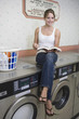 Portrait of young woman sitting on washing machine
