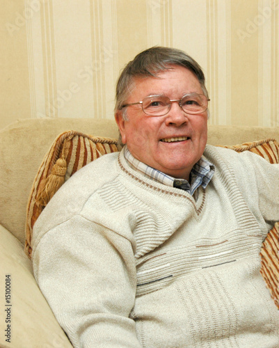 Photo: Older Man wearing glasses,smiling, sitting on sofa Older Man wearing glasses,smiling, sitting on sofa