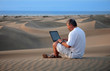 Man with laptop sitting in the desert.