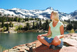 A woman sitting cross-legged next to a mountain lake.