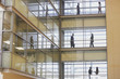 People in silhouette on multiple levels of corridor through glass
