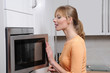 Photo: Blond woman cooks with a microwave in a modern kitchen Blond woman cooks with a microwave in a modern kitchen