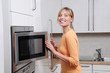 Photo: Blond woman cooks with a microwave in a modern kitchen Blond woman cooks with a microwave in a modern kitchen