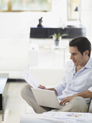 Photo: Man working on his laptop while relaxing at home Man working on his laptop while relaxing at home