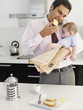 Father eating toast while holding baby daughter in a kitchen