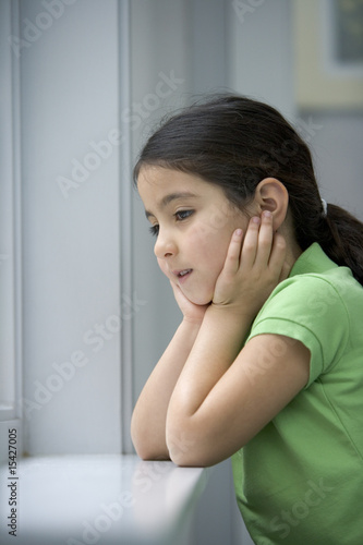 Photo: Sad little girl is looking out the window Sad little girl is looking out the window