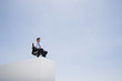 Businessman in office chair on wall outdoors with blue sky