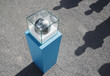 Globe in glass box on pedestal with four long shadows outdoors