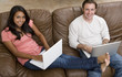 Foto: A young couple relaxing on the couch while on the computer A young couple relaxing on the couch while on the computer