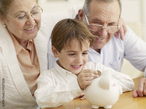 Photo: Grandparents teaching grandson to save money in a piggy bank Grandparents teaching grandson to save money in a piggy bank