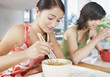 Teenage girls eating bowl of noodles with chopsticks in cafeteria