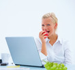 Beautiful business woman eating apple by laptop at desk