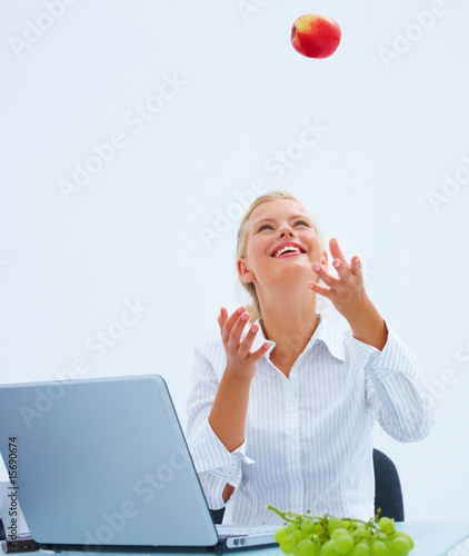 Foto: Pretty business woman playing with a apple by laptop at desk Pretty business woman playing with a apple by laptop at desk