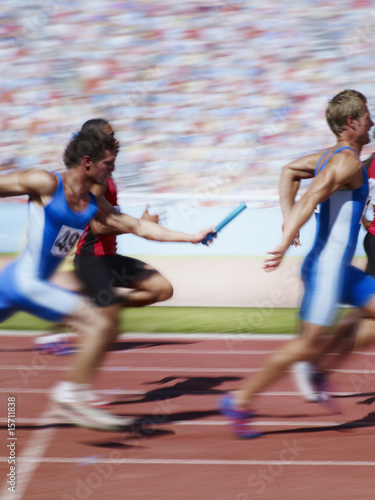 Photo: Racers running on track with relay baton Racers running on track with relay baton