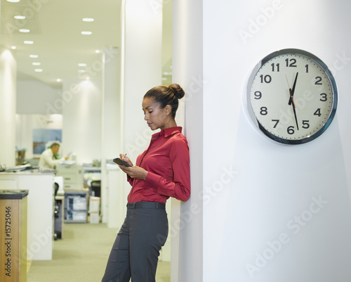 Foto: Businesswoman in office using PDA near a clock Businesswoman in office using PDA near a clock