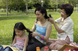 Three generations of women in park braiding each other's hair