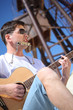 guy in sunglasses plays guitar and  lip accordion sitting on san