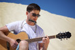 guy in sunglasses plays guitar and  lip accordion sitting on san