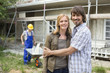 Young couple at site embracing, construction worker in background