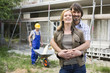 Young couple at site embracing, construction worker in background