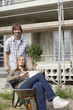 Young couple at construction site, woman sitting in wheelbarrow