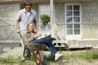 Young couple at construction site, man pushing woman in wheelbarrow