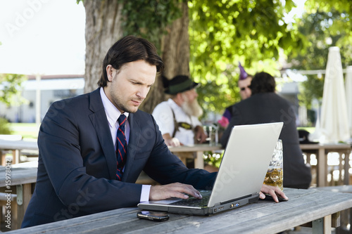 Photo: Germany, Bavaria, Upper Bavaria, Young business man in beer garden using laptop Germany, Bavaria, Upper Bavaria, Young business man in beer garden using laptop