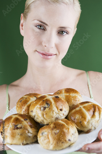 Photo: A young woman holding a plate of hot cross buns A young woman holding a plate of hot cross buns